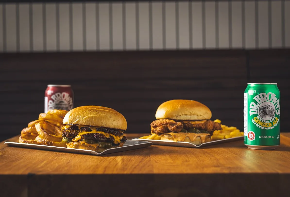 Two smash burgers with onion rings, fries and Dr. Brown's soda