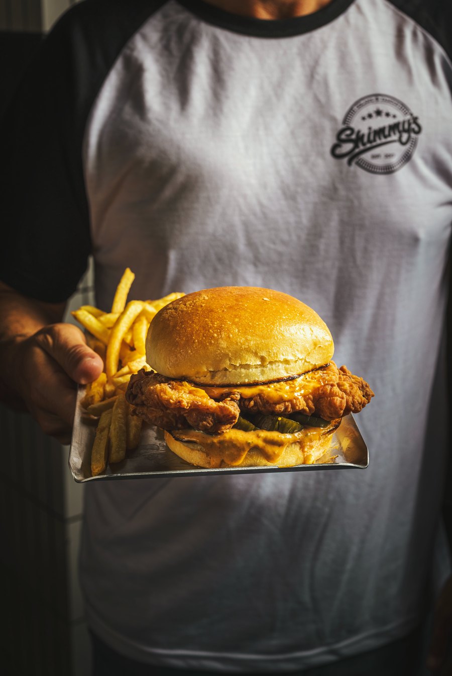 Shimmy's staff member holding a crispy chicken sandwich and fries